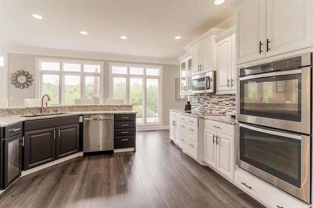 kitchen with stainless steel appliances, a sink, white cabinets, ornamental molding, and dark wood-type flooring