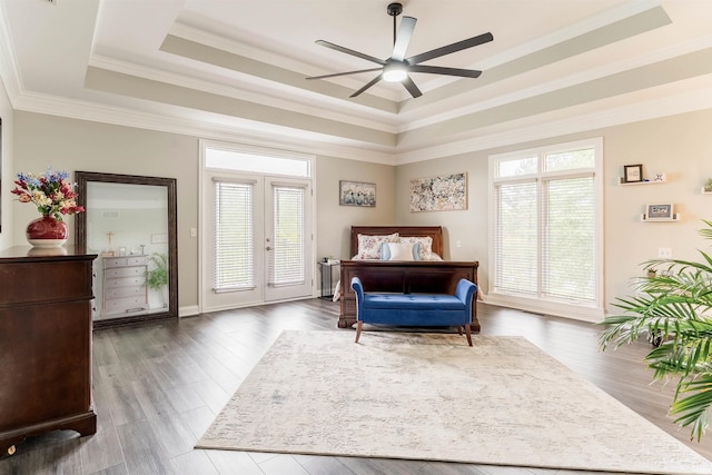 bedroom featuring multiple windows, a tray ceiling, wood finished floors, ornamental molding, and access to outside
