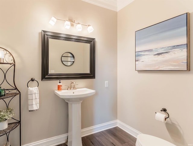 half bath with baseboards, wood finished floors, toilet, a sink, and ornamental molding