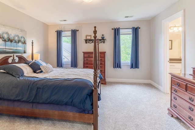 bedroom featuring multiple windows, light carpet, baseboards, and connected bathroom