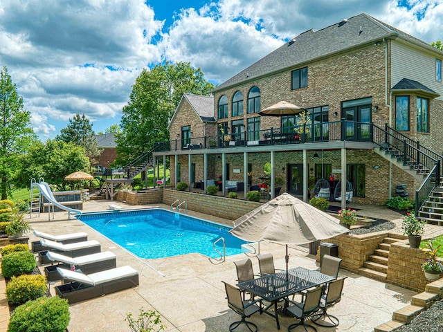 outdoor pool featuring stairway, a water slide, a patio, and a wooden deck