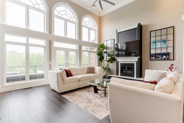 living room featuring plenty of natural light, a ceiling fan, a glass covered fireplace, ornamental molding, and dark wood-style floors