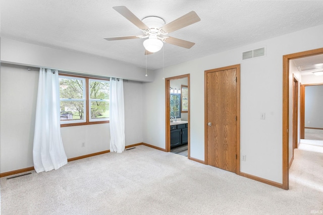 unfurnished bedroom with light carpet, baseboards, ensuite bath, ceiling fan, and a textured ceiling