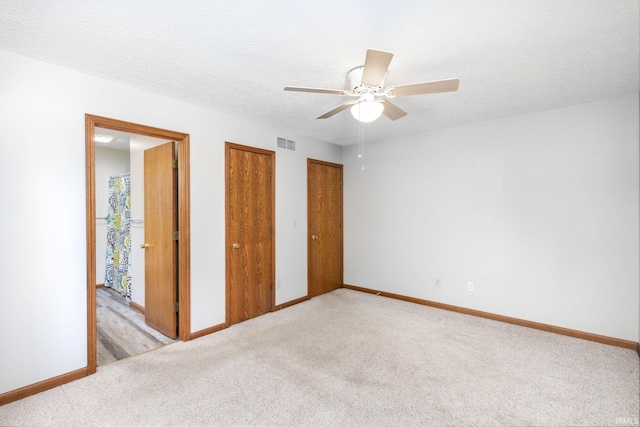 unfurnished bedroom featuring light carpet, baseboards, multiple closets, and a textured ceiling