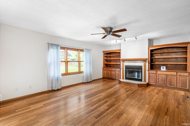unfurnished living room with light wood-style flooring, a glass covered fireplace, ceiling fan, track lighting, and baseboards