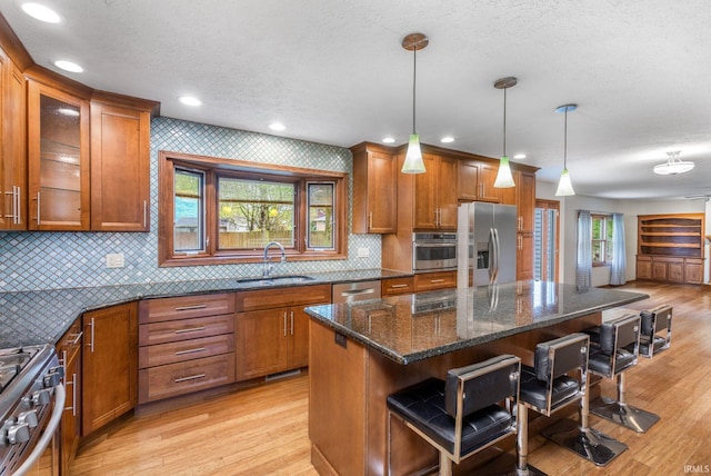 kitchen featuring a sink, stainless steel appliances, brown cabinets, a kitchen bar, and light wood finished floors