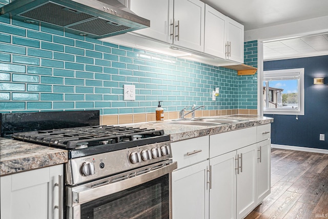 kitchen with stainless steel gas range oven, wall chimney range hood, wood finished floors, decorative backsplash, and white cabinetry