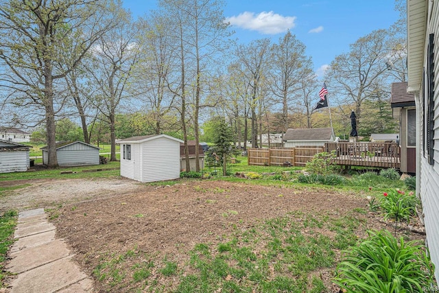 view of yard with a shed, an outbuilding, a wooden deck, and fence