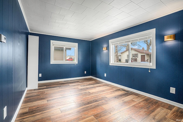 unfurnished room featuring plenty of natural light, hardwood / wood-style flooring, ornamental molding, wood walls, and baseboards