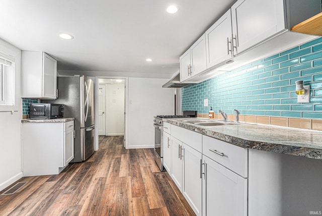 kitchen with appliances with stainless steel finishes, a sink, backsplash, dark wood-style flooring, and white cabinetry
