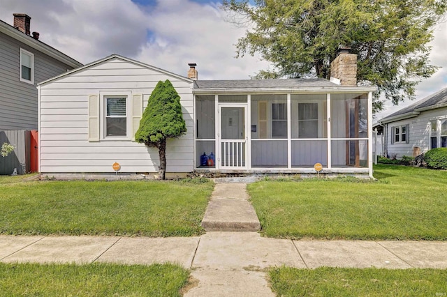 view of front of house with a sunroom, a chimney, and a front yard