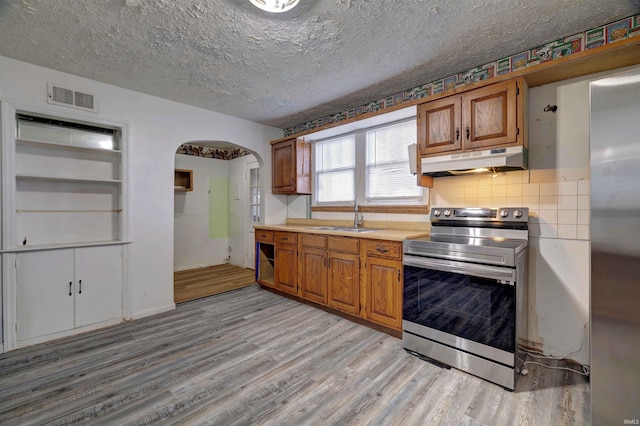 kitchen with appliances with stainless steel finishes, a sink, arched walkways, under cabinet range hood, and light wood-type flooring