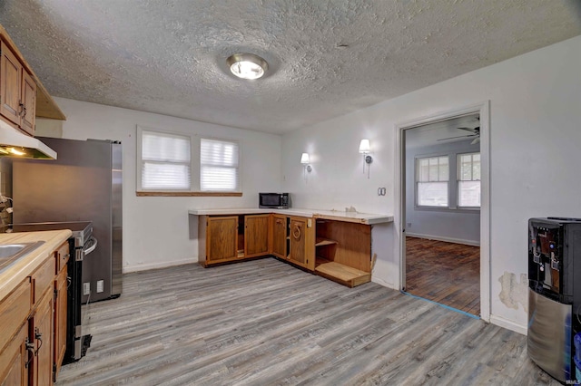 kitchen featuring light wood-type flooring, brown cabinetry, light countertops, a textured ceiling, and electric stove