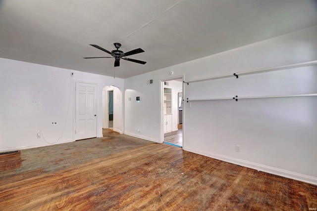 unfurnished living room with arched walkways, a ceiling fan, baseboards, and wood finished floors