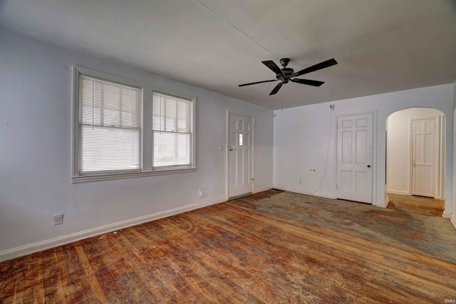 unfurnished living room featuring arched walkways, ceiling fan, wood finished floors, and baseboards