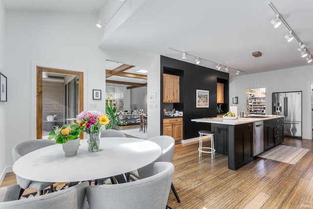 kitchen with track lighting, appliances with stainless steel finishes, a sink, a kitchen island with sink, and a breakfast bar