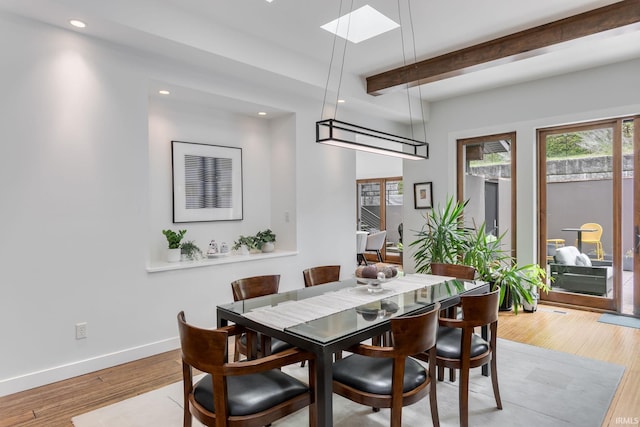 dining area with beam ceiling, a skylight, baseboards, light wood finished floors, and recessed lighting