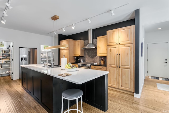kitchen featuring track lighting, wall chimney range hood, light brown cabinetry, and a sink