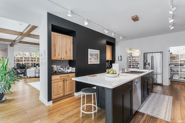 kitchen with rail lighting, stainless steel appliances, a sink, a kitchen island with sink, and light wood-type flooring