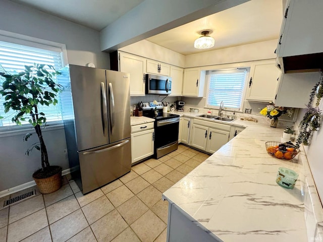 kitchen with stainless steel appliances, a sink, light tile patterned floors, light countertops, and white cabinets