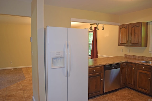 kitchen featuring white refrigerator with ice dispenser, dishwasher, light tile patterned floors, a sink, and baseboards