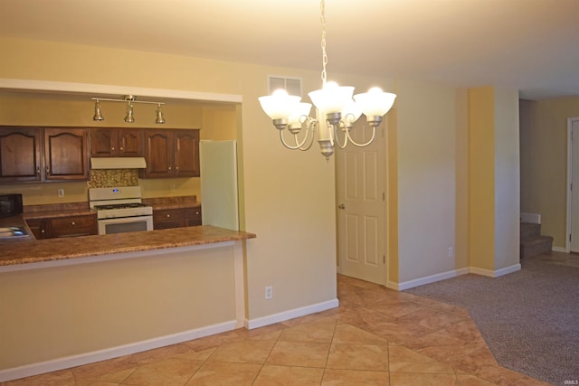 kitchen with white gas range, a chandelier, under cabinet range hood, pendant lighting, and baseboards