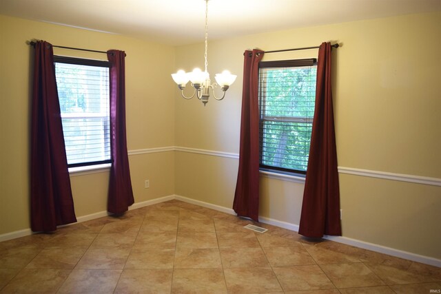 spare room featuring a chandelier, light tile patterned flooring, and baseboards