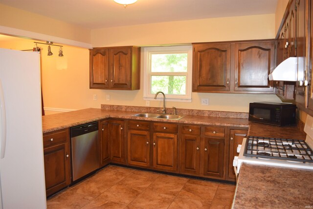 kitchen featuring white appliances, a sink, under cabinet range hood, a peninsula, and brown cabinetry
