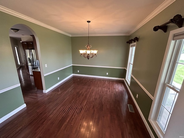 unfurnished room with wood finished floors, baseboards, ornamental molding, arched walkways, and a chandelier