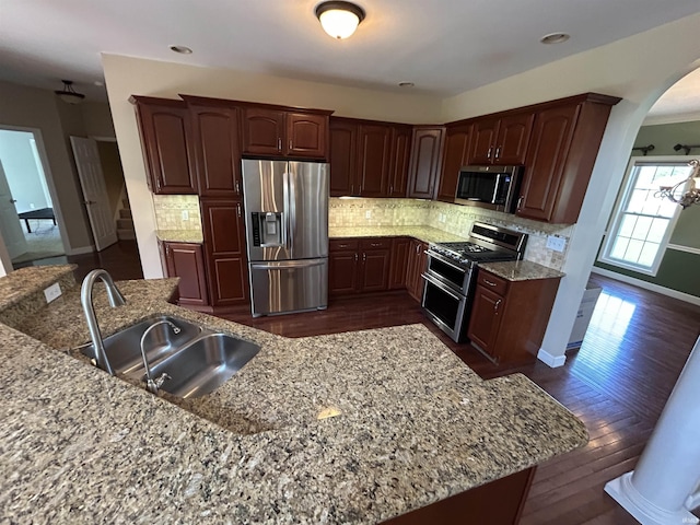 kitchen with appliances with stainless steel finishes, a sink, arched walkways, dark wood-style flooring, and recessed lighting