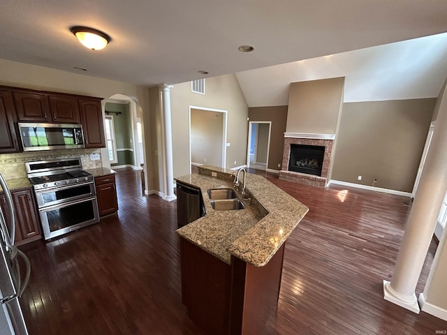 kitchen with stainless steel appliances, a sink, decorative columns, arched walkways, and a fireplace