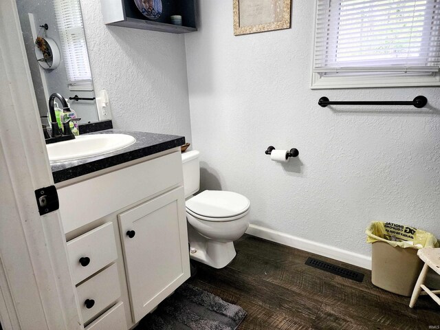 bathroom featuring toilet, wood finished floors, vanity, baseboards, and a textured wall