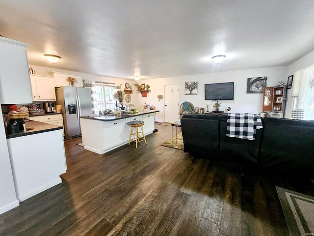 kitchen featuring stainless steel refrigerator with ice dispenser, dark countertops, dark wood-style flooring, a kitchen breakfast bar, and open floor plan