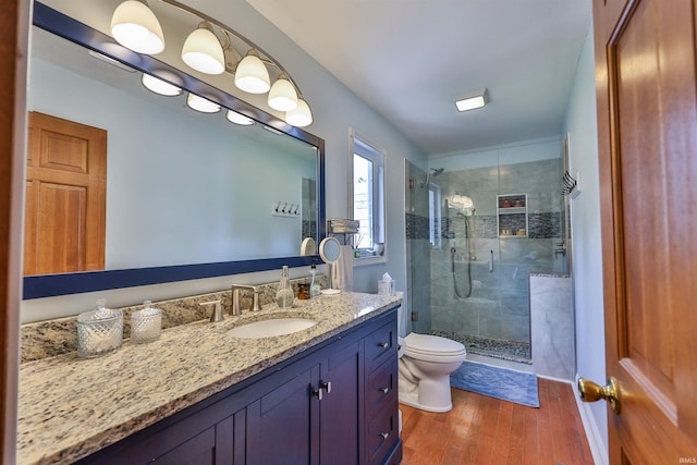 bathroom featuring toilet, vanity, a stall shower, and wood finished floors
