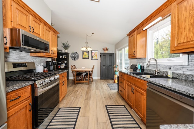 kitchen featuring appliances with stainless steel finishes, a sink, lofted ceiling, backsplash, and a chandelier