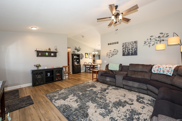living area featuring lofted ceiling, a ceiling fan, wood finished floors, baseboards, and a chandelier