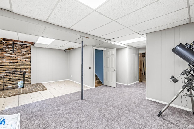 finished below grade area with a paneled ceiling, carpet flooring, stairway, baseboards, and tile patterned floors