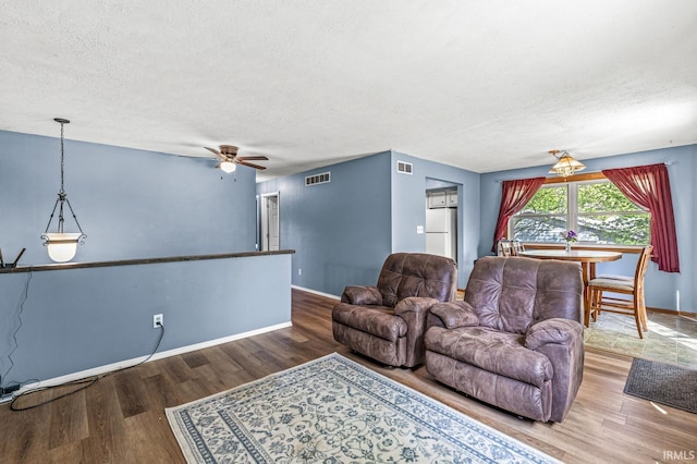 living room with a textured ceiling, wood finished floors, baseboards, and ceiling fan