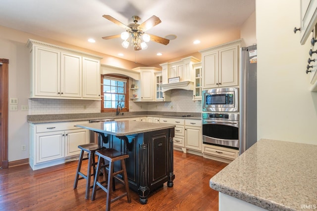 kitchen featuring stainless steel appliances, ceiling fan, dark wood-type flooring, a breakfast bar, and decorative backsplash