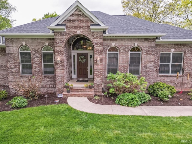 view of front of home featuring roof with shingles, brick siding, and a front lawn