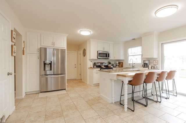 14375 Pheasant Ct, Mishawaka, IN 46545 - kitchen with stainless steel appliances, a sink, a breakfast bar area, white cabinets, and light tile patterned flooring