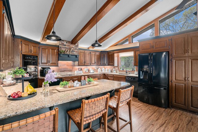 kitchen featuring black appliances, a sink, a peninsula, a breakfast bar, and light wood finished floors
