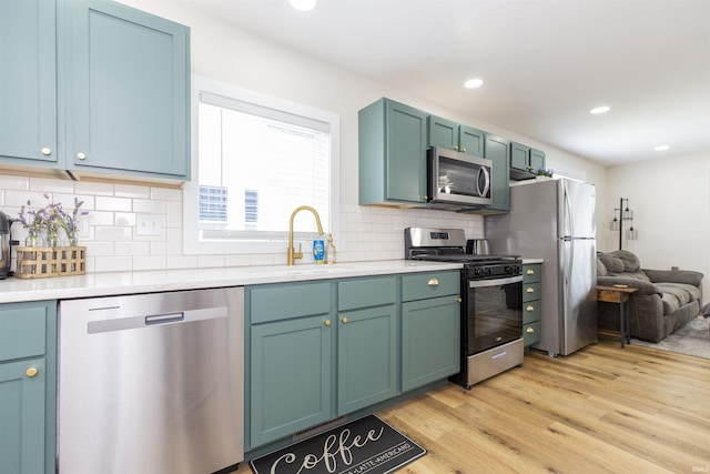 kitchen featuring stainless steel appliances, a sink, light wood-style flooring, light countertops, and decorative backsplash