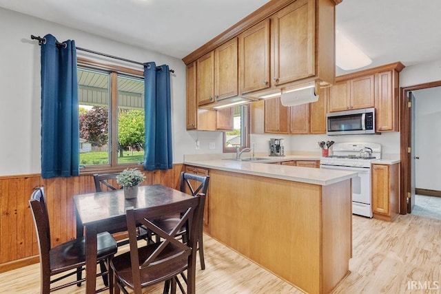 kitchen featuring stainless steel microwave, white gas range oven, a sink, light countertops, and a peninsula