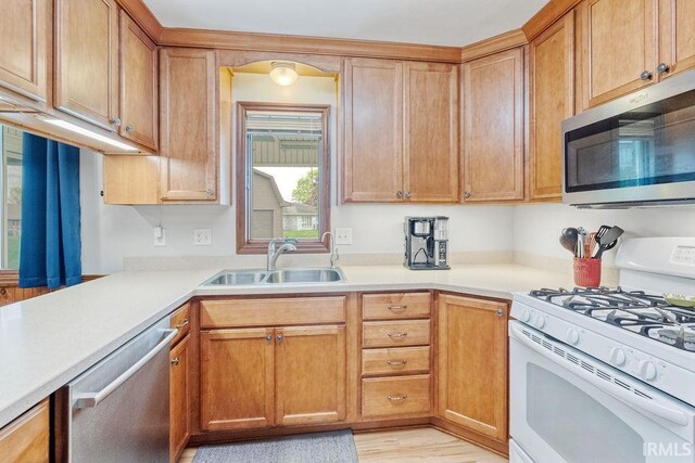 kitchen with appliances with stainless steel finishes, a sink, light countertops, light wood-type flooring, and brown cabinetry