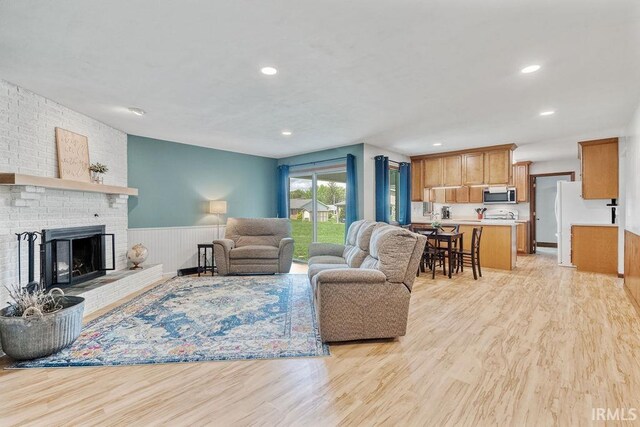 living room featuring light wood-style floors, a wainscoted wall, a brick fireplace, and recessed lighting