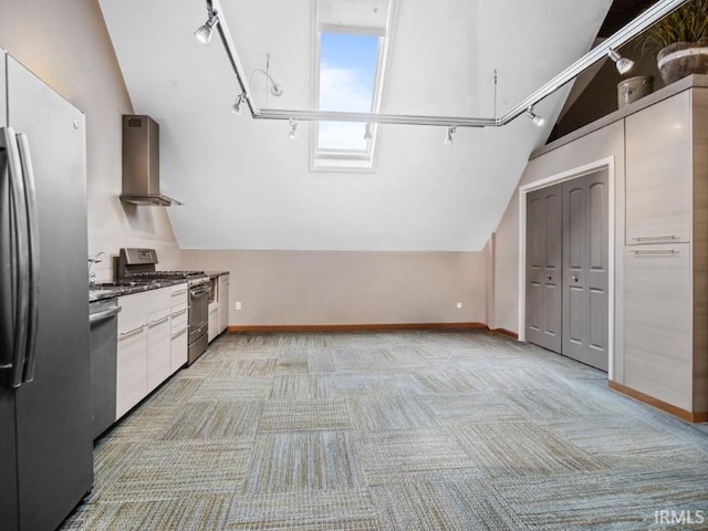kitchen featuring stainless steel appliances, wall chimney range hood, vaulted ceiling, rail lighting, and light colored carpet