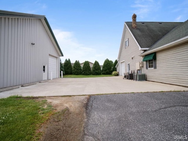 view of property exterior featuring board and batten siding, a garage, a chimney, and cooling unit