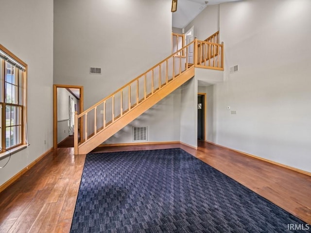 stairway featuring wood finished floors, a towering ceiling, and baseboards