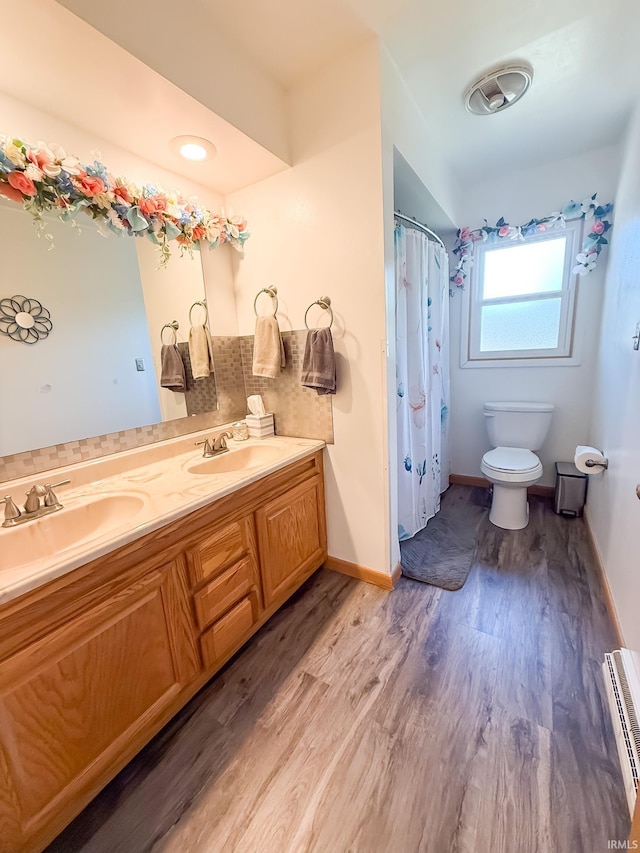 full bath with a baseboard radiator, toilet, wood finished floors, double vanity, and baseboards